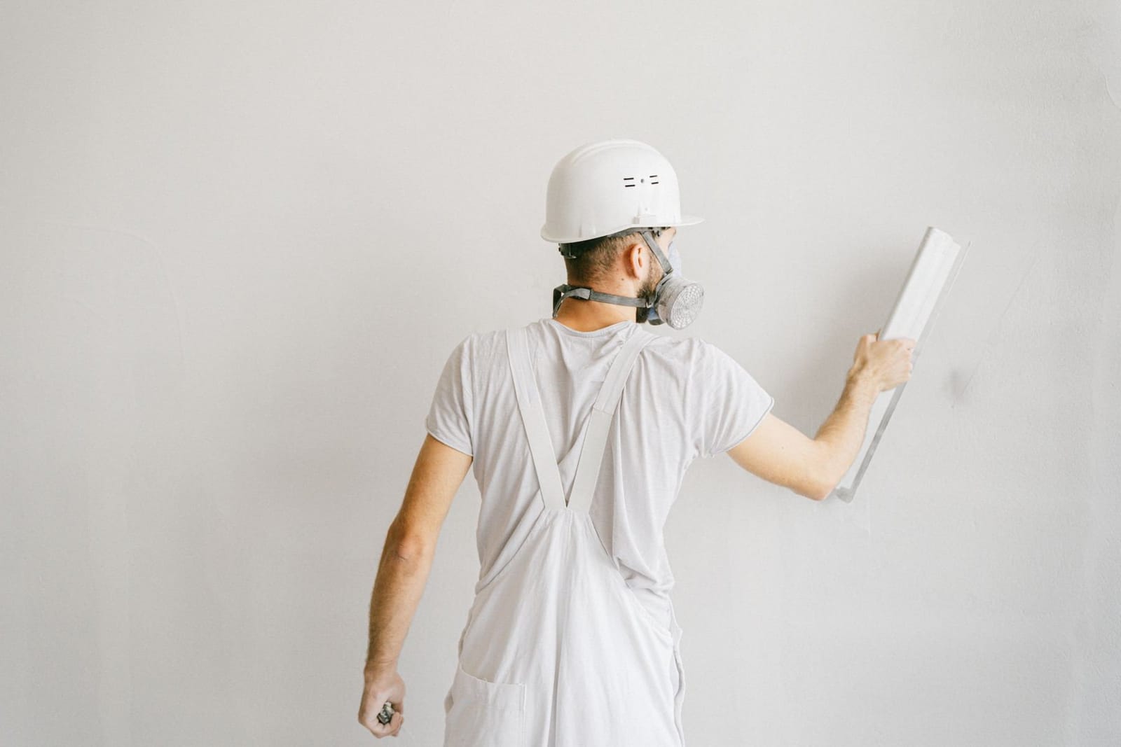 Professional painter in white overalls, hard hat, and respirator skim-coating a wall during prep work on a Hudson Valley home